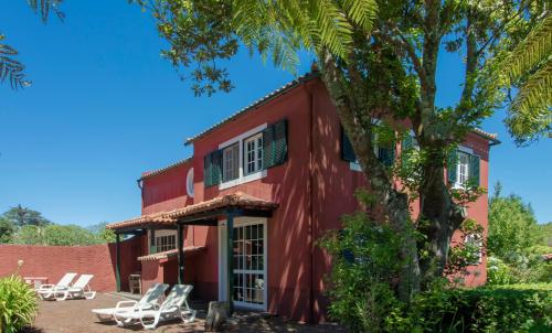 een rood huis met stoelen en een boom bij Quinta Santo Antonio Da Serra in Santa Cruz