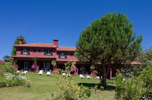 een groot rood huis met stoelen en een boom bij Quinta Santo Antonio Da Serra in Santa Cruz