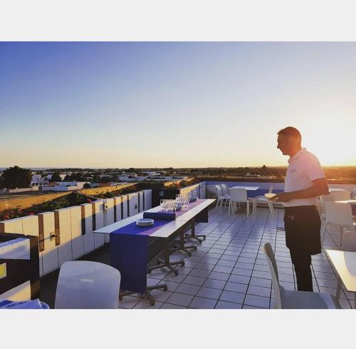 Ein Mann steht auf einem Balkon mit Tischen und Stühlen in der Unterkunft L'Angolo Di Beppe in Torre Lapillo