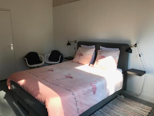 1 Schlafzimmer mit einem Bett mit rosa Bettwäsche und 2 Stühlen in der Unterkunft Bij Zelle in Garderen