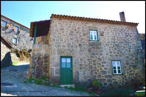 um edifício de pedra com uma porta verde e janelas em Castelo Cottages II em Monsanto