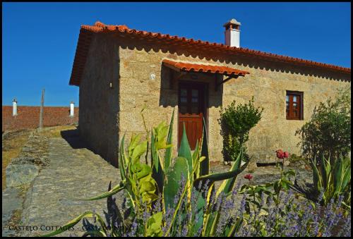 een stenen huis met een rode deur en wat bloemen bij Castelo Cottages in Castelo Novo