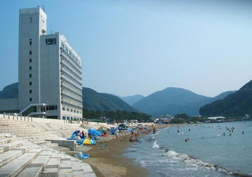 un groupe de personnes sur une plage avec un bâtiment dans l'établissement Nishiizu Matsuzaki Itoen Hotel, à Matsuzaki