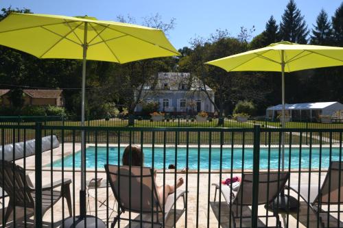 une femme assise dans des chaises longues sous des parasols à côté d'une piscine dans l'établissement Hôtel les Grands Chênes, à Saint-Fargeau