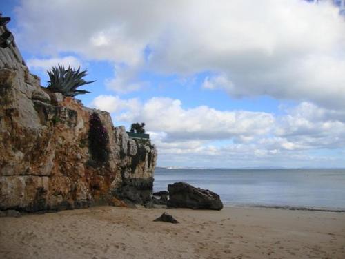 een strand met een rotswand en de oceaan bij Suites Guest House in Cascais