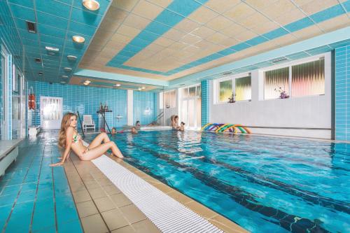 a woman sitting on the edge of a swimming pool at Hotel Ambra in Luhačovice