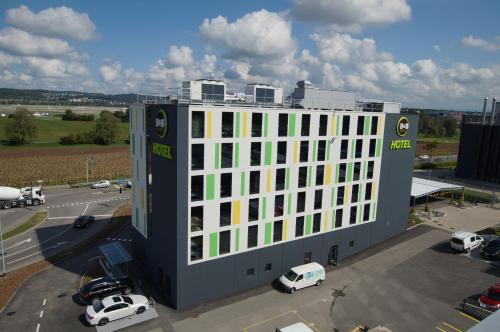 een groot wit gebouw met auto's geparkeerd op een parkeerplaats bij B&B HOTEL Zürich Airport in Rümlang