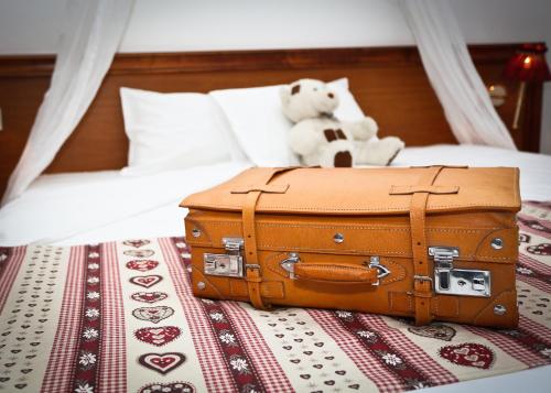 un ours en peluche et une valise sur un lit dans l'établissement The Originals Boutique, Hôtel La Ferme du Pape, Eguisheim, à Eguisheim