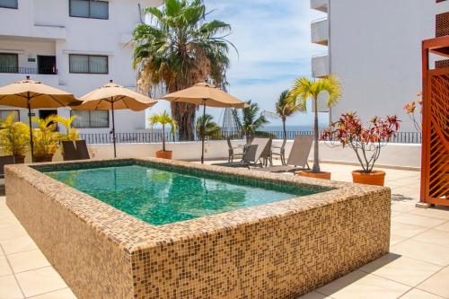 a swimming pool in a resort with chairs and umbrellas at Amapas Apartments Puerto Vallarta in Puerto Vallarta