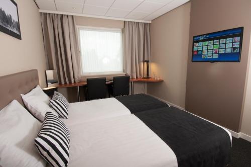 a bedroom with a bed and a desk and a window at Hotel De Zoete Inval Haarlemmerliede in Haarlem