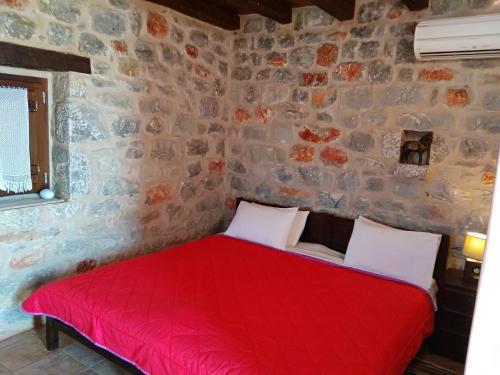 - une chambre avec un lit rouge dans un mur en pierre dans l'établissement Pirgoi Edem, à Pirgos Dhirou