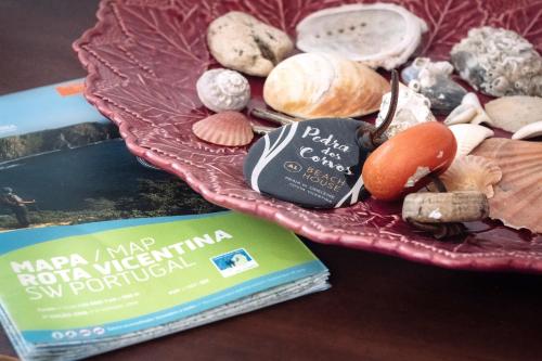 a book and some shells on a pink plate at PEDRA DOS CORVOS Beach House in Odeceixe