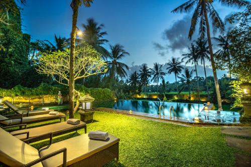 乌布Ananda Ubud Resort的夜间带长凳和棕榈树的度假游泳池