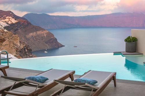 een zwembad met stoelen en uitzicht op het water bij Aloia Villas in Oia