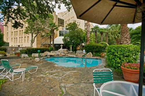 einen Pool mit Stühlen, einem Tisch und einem Sonnenschirm in der Unterkunft The Crockett Hotel in San Antonio