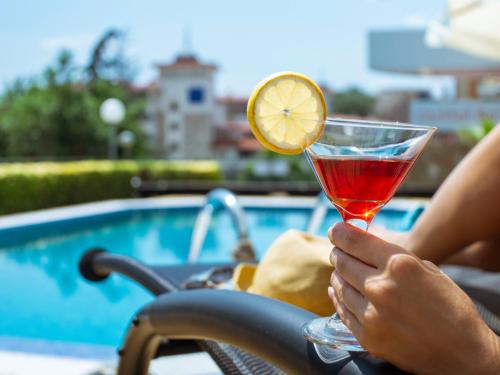 uma pessoa que segura uma bebida em frente a uma piscina em Milennia Family Hotel em Sunny Beach