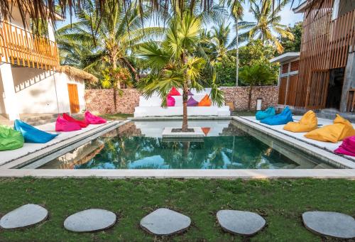 una piscina con almohadas coloridas y una palmera en Kaniu Capsule Hostel, en Kuta Lombok