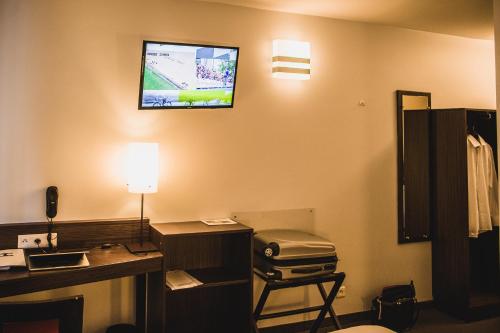 um quarto com uma secretária e uma televisão na parede em DC Hotel Charleroi Airport em Charleroi