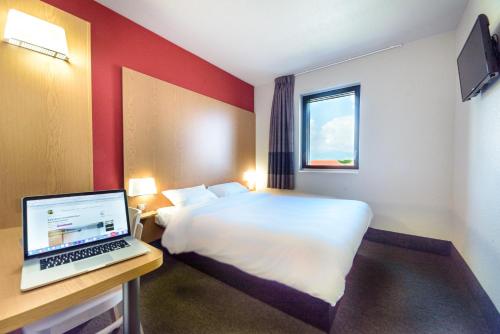 ein Hotelzimmer mit einem Bett und einem Laptop auf dem Schreibtisch in der Unterkunft B&B HOTEL Colmar Expo in Colmar