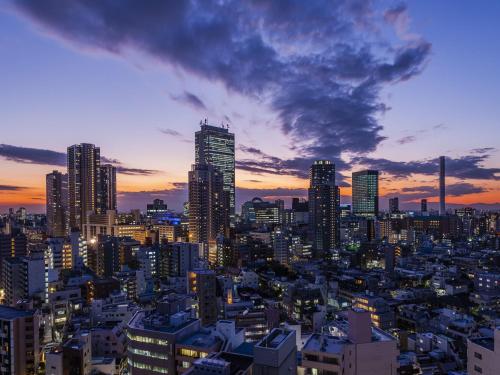 APA Hotel Yamanote Otsuka Eki Tower في طوكيو: أفق المدينة عند غروب الشمس مع المباني الطويلة