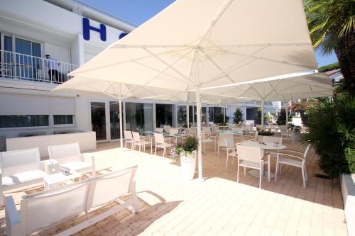 een patio met witte tafels, stoelen en parasols bij Hôtel Josse in Antibes