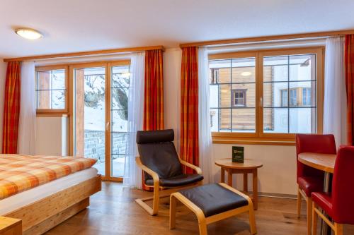 een slaapkamer met een bed, een stoel en ramen bij Jägerhof Serviced Apartements in Zermatt