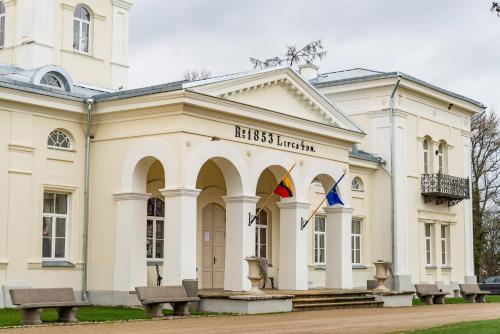 a white building with benches in front of it at Burbiskio dvaras in Anykščiai