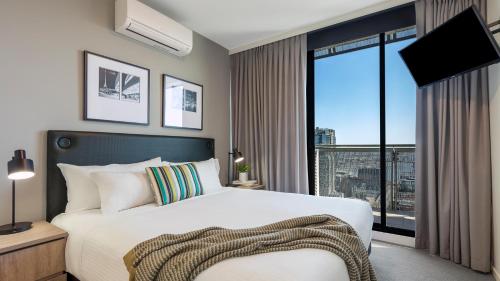 Oaks Melbourne on William Suites في ملبورن: غرفة نوم بسرير ونافذة كبيرة