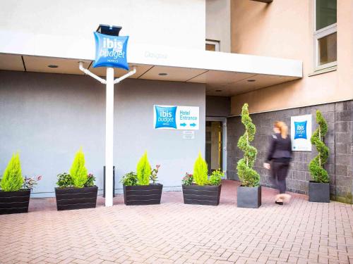 une personne marchant devant un bâtiment avec des plantes dans l'établissement ibis budget Glasgow, à Glasgow