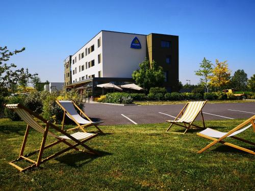 drei Stühle im Gras vor einem Gebäude in der Unterkunft Akena City Reims Bezannes in Reims