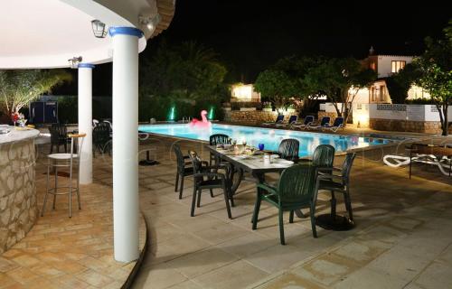 uma mesa e cadeiras ao lado de uma piscina à noite em CASA BEACHCOMBER Le jardin des Arts em Lagos