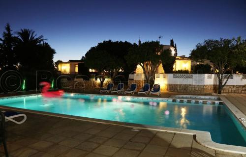 uma piscina à noite com cadeiras à volta em CASA BEACHCOMBER Le jardin des Arts em Lagos