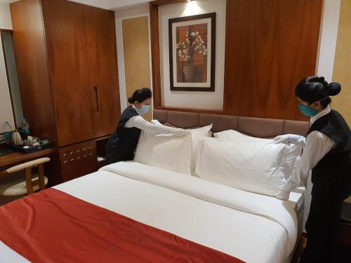 two women wearing masks making a bed in a hotel room at Hotel MBC Citadel Nashik in Nashik