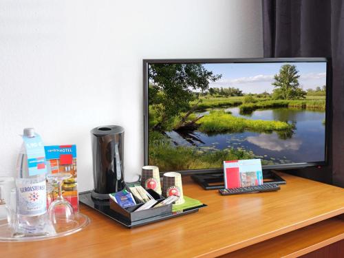 a television sitting on a desk with cosmetics and a drink at centra Hotel in Schwedt