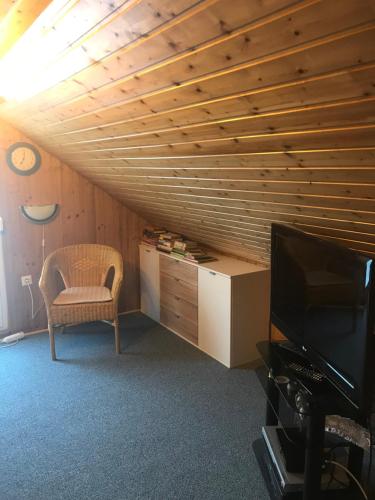 Cette chambre dispose d'un plafond en bois, d'une chaise et d'une télévision. dans l'établissement Ferienwohnung Gürth, à Kleinhennersdorf