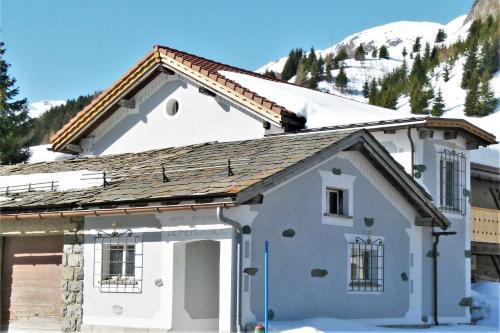 ein weißes Haus mit verschneiten Bergen im Hintergrund in der Unterkunft Ferienwohnung Grischuna in Bivio