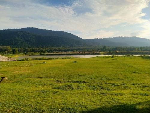 um campo verde com um rio e montanhas ao fundo em Samerdrow Khao Yai em Mu Si