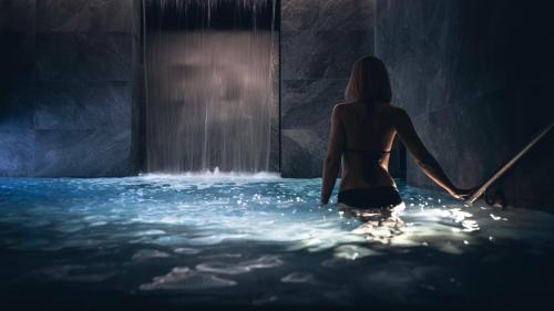 une femme debout dans l'eau devant une cascade dans l'établissement Le Parc Hôtel Obernai & Yonaguni Spa, à Obernai