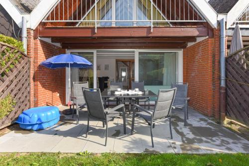 um pátio com uma mesa, cadeiras e um guarda-sol em Ferienhaus Nordlicht em Bensersiel