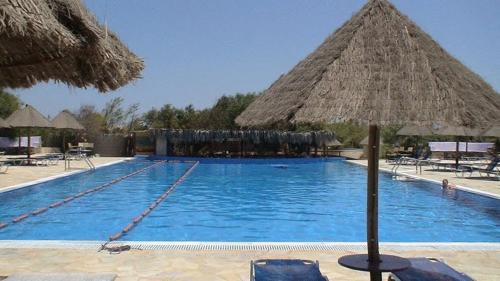 una grande piscina con ombrellone e sedie di paglia di Surfing Beach Huts a Santa Maria