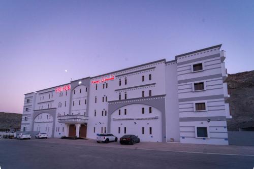 a large white building with cars parked in a parking lot at Riyam Hotel in Muscat