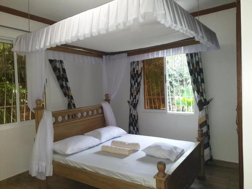 una camera con letto a baldacchino con lenzuola e cuscini bianchi di Karibuni palace mtwapa a Mtwapa