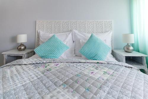 a white bed with two blue pillows and two tables at Aurora Vendégház in Hévíz