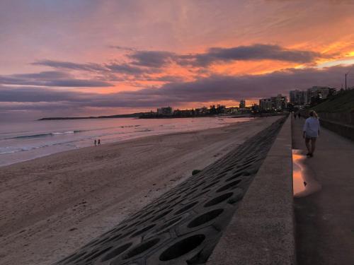 uma mulher andando numa praia com pegadas na areia em Lautan Cronulla Beach em Cronulla