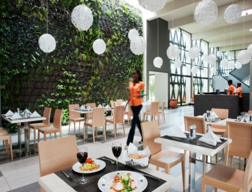 una donna che cammina in un ristorante con tavoli e sedie di ONOMO Hotel Libreville a Libreville