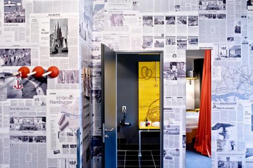 a hallway with a wall covered in newspapers at Superbude Hamburg St Pauli in Hamburg