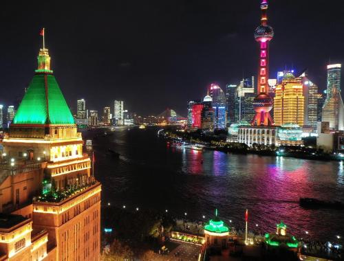 um horizonte da cidade à noite com um rio e edifícios em Fairmont Peace Hotel on the Bund em Xangai