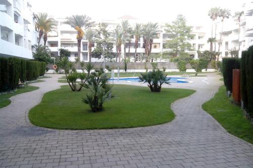 a walkway through a park with palm trees and a building at Bonito apartamento de 3 hab. con jardín in Roses