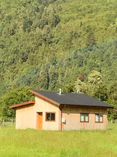 una pequeña casa con un techo negro en un campo en Cabañas Río del Este SPA, en Puerto Varas