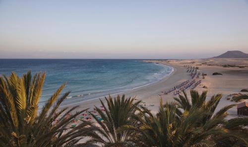 a beach with a bunch of people and the ocean at Hotel Riu Palace Tres Islas in Corralejo